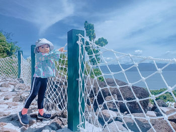 Portrait of cute girl standing by net against sky