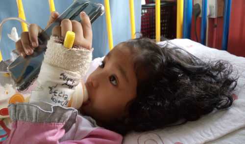 Cute injured girl using phone while lying on hospital bed