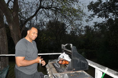 Portrait of mature man preparing food on barbecue grill against trees at dusk