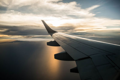 Airplane flying over sea against sky during sunset