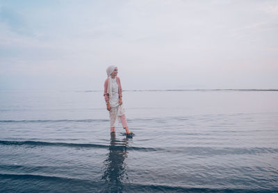 Woman wading in sea against sky