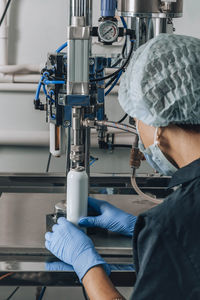 A woman in a mask, cap and gloves works in the production of cosmetics or a pharmaceutical company