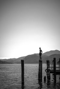 Man standing on wooden post by lake against sky