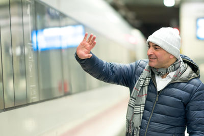 Man waving hand while standing at railroad station platform