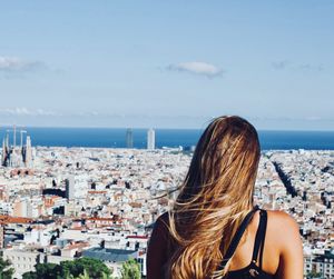 Rear view of woman looking at cityscape against sky