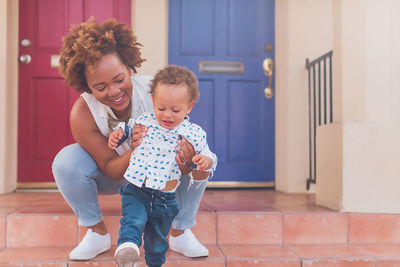 Mom and toddler helping son walk down the steps on front porch