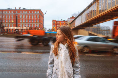 Young woman by car on road against sky in city