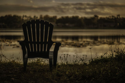 Empty chairs by lake against sky during sunset