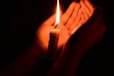 Close-up of hand holding lit candle in darkroom