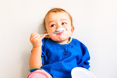Portrait of cute boy eating while sitting against white background