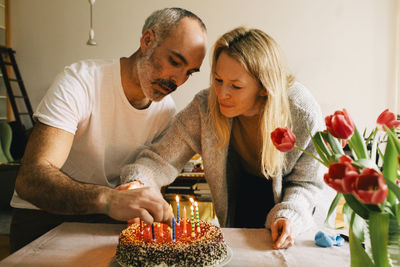 Couple arranging candles on birthday cake together at home