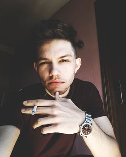Portrait of young man holding cigarette at home