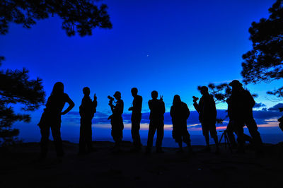 Silhouette people standing at beach against clear blue sky