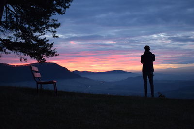 Silhouette man photographing on landscape against sky during sunset