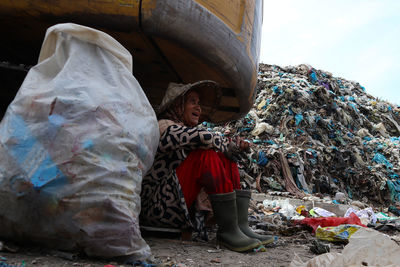 Midsection of man sitting by garbage against sky