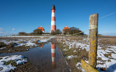 Lighthouse by sea against clear blue sky