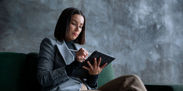 Young female designer sitting on green sofa in loft living room and drawing on tablet computer