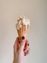 Cropped image of hand holding ice cream cone against white background
