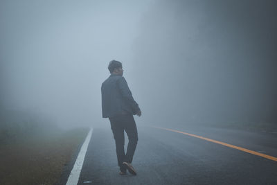 Rear view of man standing on road during foggy weather