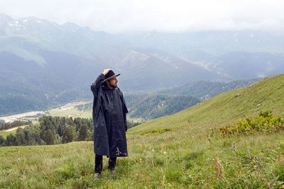 Man with a beard shepherd standing in the mountains in a black raincoat in the rain