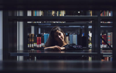 Portrait of young woman seen through bookshelves at library