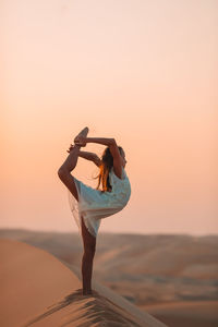 Woman with umbrella standing on land against sky during sunset