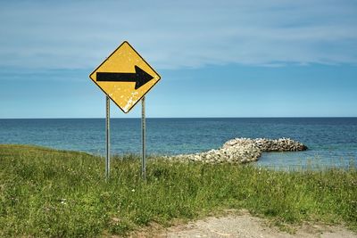 Road sign by sea against sky