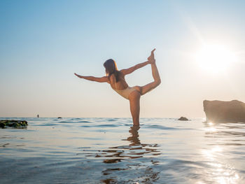 Woman doing yoga in sea against sky