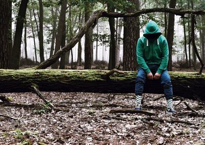 Full length of man sitting on fallen tree in forest