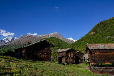 Houses on field by mountains against blue sky