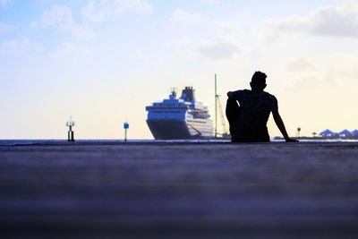 Rear view of silhouette man sitting at harbor against sky during sunset