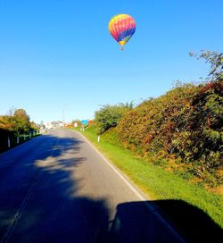 Hot air balloon flying over road against clear blue sky