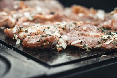  grilling pork neck meat on a granite stone laid on heat of fire. meat sprinkled with salt, basil