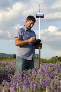 Surveyor using equipment on lavender field against cloudy sky