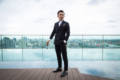 Full length of young man standing at swimming pool against sky