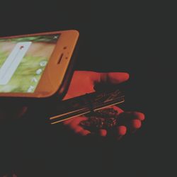 Close-up of hand holding mobile over black background