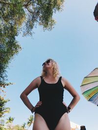 Low angle view of woman in swimwear standing with hands on hip against clear sky