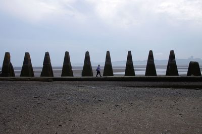 Woman walking by rock formations at beach against sky