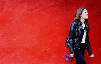Portrait of young woman standing against red wall
