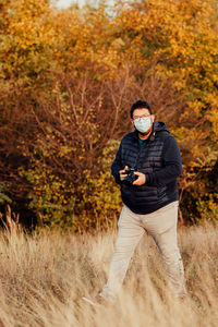 Man photographer standing on field during autumn and shooting a photo session