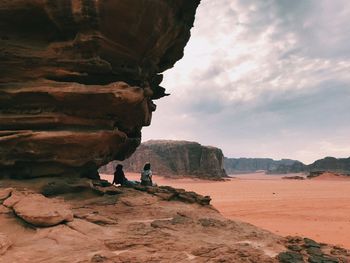 People on rock by mountain against sky