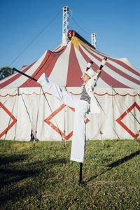 Male artist holding juggling pins while performing with stilts on meadow