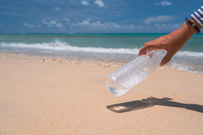 Midsection of person hand on sand at beach against sky