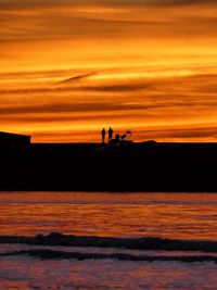 Silhouette people on beach against dramatic sky during sunset