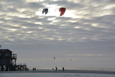 Kiteboarding at beach against cloudy sky