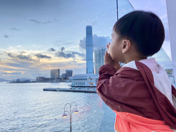 Side view of asian boy looking at sea against sky during sunset