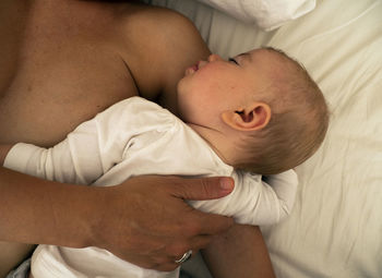 High angle view of sensuous mother breastfeeding baby sleeping on bed