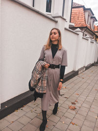 Full length of woman standing on footpath against wall