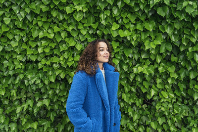 Beautiful young woman standing against green plants