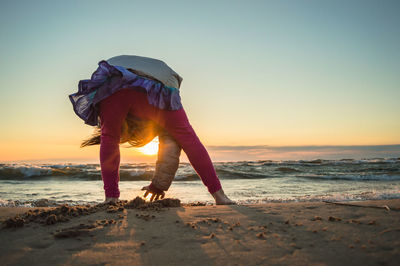 Full length of girl standing on beach against sky during sunset
